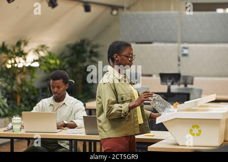 Seitenansicht Porträt einer jungen afroamerikanischen Frau, die Papierbecher in die Abfallsortiertonne im Büro legt, Kopierraum Stockfoto