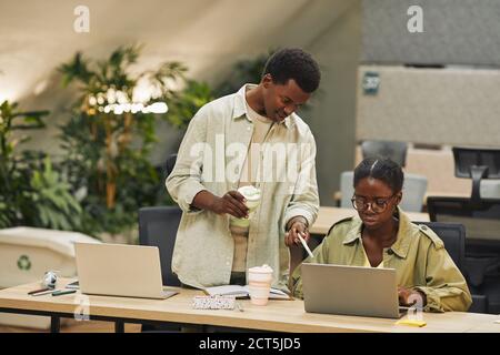 Portrait von zwei afroamerikanischen Menschen arbeiten in modernen Open Space Büro, konzentrieren sich auf junge Mann instruiert Kollegen und zeigt auf Laptop-Bildschirm , Kopierer Raum