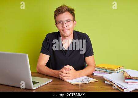 Selbstbewusster kaukasischer männlicher Chef mit Laptop am Schreibtisch, sitzt er und schaut auf die Kamera, hält Interview für Mitarbeiter. Isolierter grüner Hintergrund Stockfoto