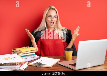 Verärgerte Frau Blick auf Laptop, unzufrieden mit dem Ergebnis auf der Arbeit. Wütend weiblich fühlen sich unglücklich, isoliert roten Hintergrund Stockfoto