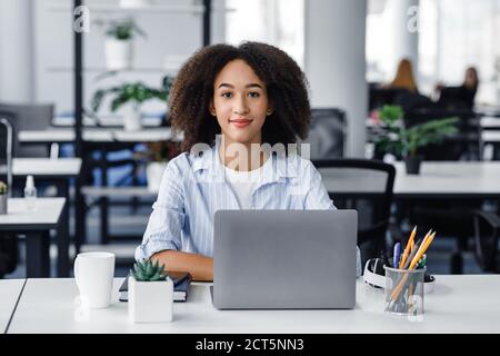 Porträt einer afroamerikanischen jungen Frau, die nach Quarantäne im Coworking-Büro arbeitet. Freundliche Dame, die am Computer am Arbeitsplatz sitzt Stockfoto