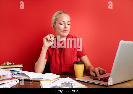 Porträt von nachdenklichen kaukasischen Frau am Arbeitsplatz, sie ist Kontemplation, mit zu viel Arbeit, Fristen. Sitzen mit Laptop isoliert über roten Backgr Stockfoto
