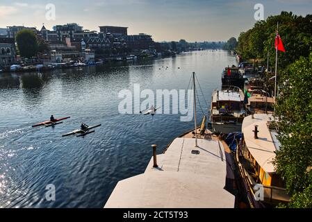 Kanus fahren die Themse entlang, vorbei an Hausbooten in der Nähe der Kingston Bridge und der Uferpromenade von Kingston upon Thames im Großraum London Stockfoto