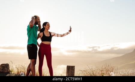 Fitnesspaar steht draußen und macht nach dem Training ein Selfie. Ein Paar hat Spaß, sich nach einem Lauf zu entspannen und ein Selfie über das Mobiltelefon zu machen. Stockfoto