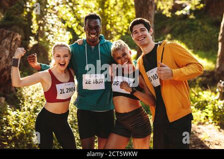 Team von Läufern feiert nach dem Gewinn des Rennens. Glückliche Marathonläufer stehen nach einem Rennen im Wald zusammen. Stockfoto