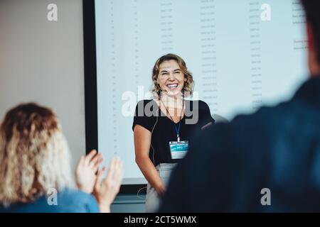 Geschäftsfrau lächelt mit Publikum, das bei einer Konferenz die Hände klatscht. Weibliche Profis bekommen Applaus von den Konferenzteilnehmern. Stockfoto