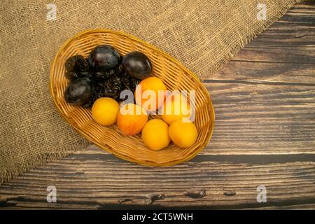 Reife Aprikosen und saftige schwarze Pflaumen in einem Weidenkorb. Nahaufnahme. Herbsternte Stockfoto