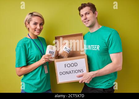 Portrait des jungen kaukasischen Paares sammeln Spende für Arme, halten Box mit Getreide isoliert auf grünem Hintergrund Stockfoto