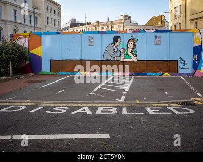 Graffiti eines Mannes, der eine Frau in einer Bar plaudert, Behindertenparkplätze im Vordergrund, Hastings England Stockfoto