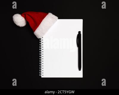 Dunkle Weihnachten flach lag mit leerem Notizbuch mit Kopierplatz für zu tun oder Wunschliste, Ziele, Neujahr Auflösung oder 2021 Plan mit Stift und roten Weihnachtsmann h Stockfoto