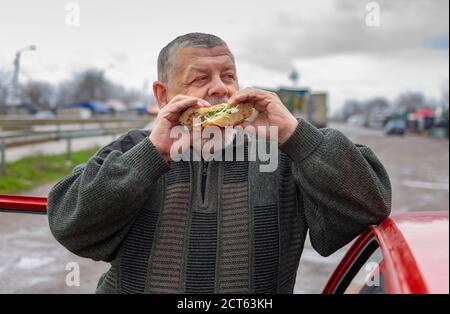 Kaukasischer Senior-Fahrer verschlingen lyulya Kebab in Lavasch lehnte seine Ellenbogen auf dem Autodach Stockfoto