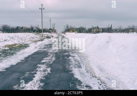 Winterlandschaft mit einer eisbedeckten Asphaltstraße im ländlichen Dorf Skelki, Saporischschja Oblast, Ukraine Stockfoto