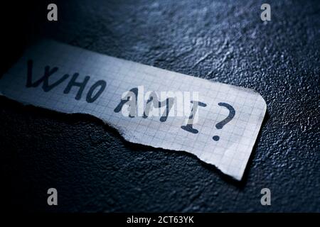 Ein Stück Papier mit der Frage, wer ich darin geschrieben bin, auf einer schwarzen strukturierten Oberfläche Stockfoto
