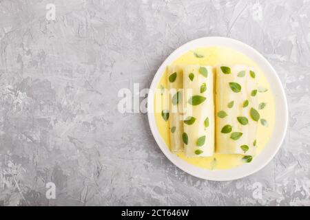 Cannelloni-Pasta mit Eiersauce, Frischkäse und Oregano-Blättern auf grauem Betonboden. Draufsicht, flach liegend, Kopierraum. Stockfoto