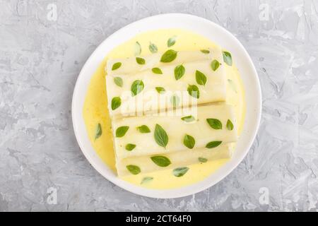 Cannelloni-Pasta mit Eiersauce, Frischkäse und Oregano-Blättern auf grauem Betonboden. Draufsicht, flach liegend, Nahaufnahme. Stockfoto