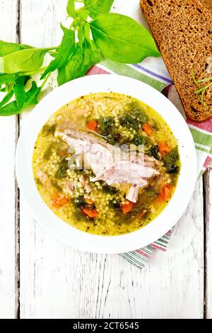 Schweinebrippen-Suppe mit Couscous und Spinat in einem Teller auf Serviette, Brot auf dem Hintergrund eines hellen Holzbretts von oben Stockfoto