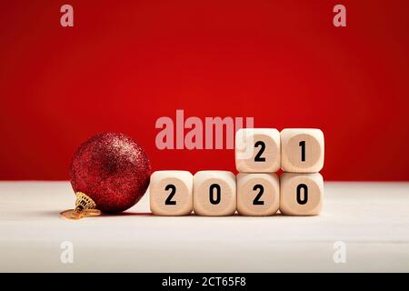 Neujahr-Konzept mit Holzblöcken mit dem Jahr 2020 und 2021 Zahlen ändern sich auf rotem Hintergrund mit einem Weihnachtsschmuck. Stockfoto