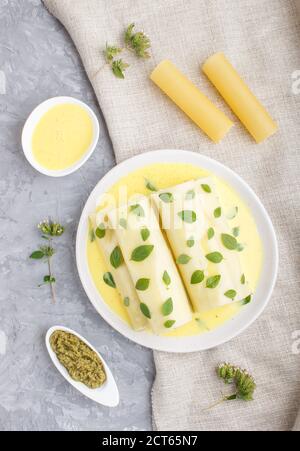 Cannelloni-Pasta mit Eiersauce, Frischkäse und Oregano-Blättern auf grauem Betonboden mit Leinentextilien. Draufsicht, flaches Lay, Nahaufnahme. Stockfoto