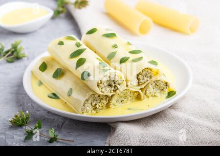 Cannelloni-Pasta mit Eiersauce, Frischkäse und Oregano-Blättern auf grauem Betonboden mit Leinentextilien. Seitenansicht, Nahaufnahme, selektiver Focu Stockfoto