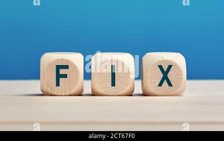 Das Wort fix auf Holzwürfel vor blauem Hintergrund. Reparatur-, Reparatur- oder Lösungskonzept. Stockfoto