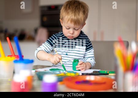 Drei Jahre alter Junge beschäftigt Malerei zu Hause, mit Farbtöpfen und Bürsten. Stockfoto