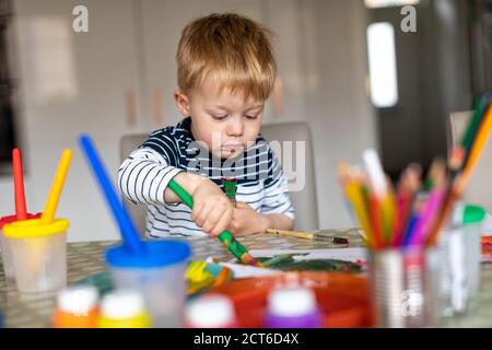 Drei Jahre alter Junge beschäftigt Malerei zu Hause, mit Farbtöpfen und Bürsten. Stockfoto