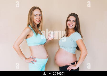 Junge schwangere Frauen im Sport tragen mit Glas Wasser Isoliert auf beigem Hintergrund Stockfoto
