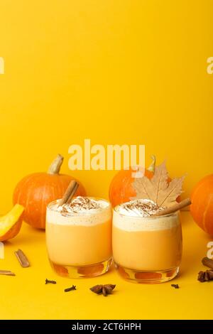 Kürbis Latte Getränk. Herbstlicher Kaffee mit würzigem Kürbisgeschmack und Sahne auf gelbem Hintergrund. Saisonale Herbstgetränke zu Halloween und Thanksgiving Stockfoto