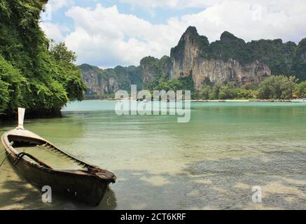 Blick auf Kalksteinfelsen über dem Railay West Beach mit altem Boot im Vordergrund in der Provinz Krabi, Thailand Stockfoto