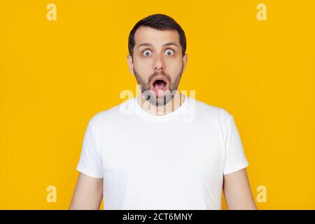 Junger Mann mit Bart in weißem T-Shirt mit offenem Mund, ängstlich und schockiert von unerwartetem Ausdruck, Angst und aufgeregt Gesicht, steht auf isoliertem gelben Hintergrund. Stockfoto