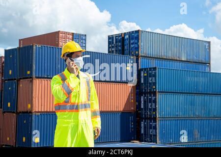 Container-Arbeiter tragen schützende Gesichtsmaske während Corona-Virus und Grippe-Ausbruch verwenden Smartphone reden an Frachtcontainer. Stockfoto