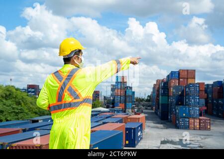 Vorarbeiter mit Schutzmaske zum Schutz vor Covid-19, der am Frachtcontainer steht. Stockfoto