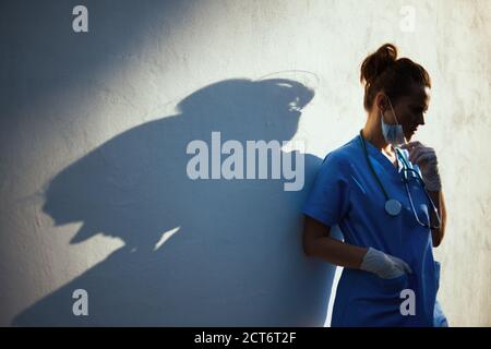 Coronavirus Pandemie. Betont moderne Arzt Frau in Scrubs mit Stethoskop, medizinische Maske und Gummihandschuhe im Freien in der Stadt in der Nähe von Wand. Stockfoto