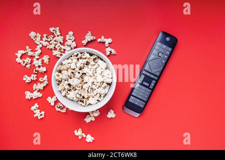 Schüssel Popcorn und TV-Fernbedienung auf rotem Hintergrund Stockfoto