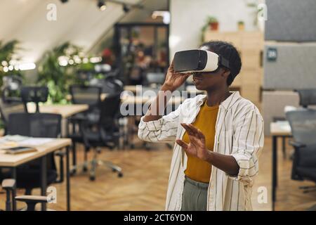 Waist up Porträt der jungen afroamerikanischen Frau trägt VR-Helm im Büro und genießen immersive Realität, kopieren Raum Stockfoto