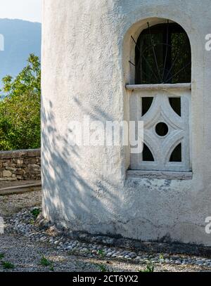 Religiöse Gebäude Außenwand Detail. Ein Fenster, das durch Balken und Betondekorationen geschützt ist. Im Hintergrund grüne Bäume Stockfoto