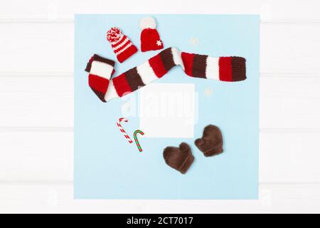 Gestrickte Hüte, Schal, Fäustlinge, Weihnachtsbonbons und Schneeflocken auf weiß getünchten Holzbrettern. Speicherplatz kopieren. Winterurlaub Grußkarte Modell Stockfoto