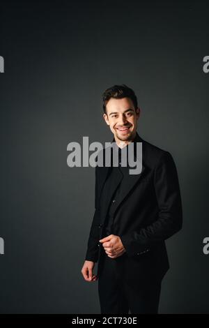 Jungen gutaussehenden Mann in einem schwarzen Anzug, lächelnd und mit Blick auf die Kamera, gegen normales studio Hintergrund Stockfoto