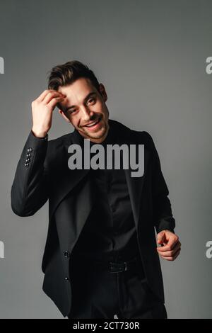 Jungen gutaussehenden Mann in einem schwarzen Anzug, Lachen, und wenn man die Kamera, gegen normales studio Hintergrund Stockfoto
