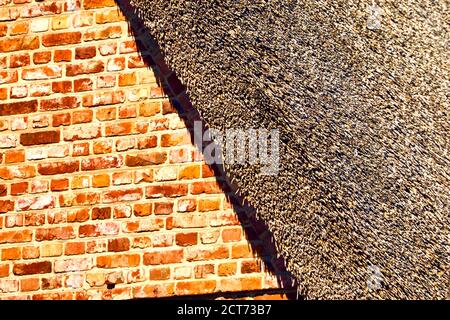 Abstrakt aussehende Teil eines Backsteinhauses mit einem Reetgedeckten Dach in der harten Mittagssonne Stockfoto