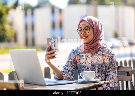 Junge muslimische Frau mit einem Laptop im Café im Freien Stockfoto