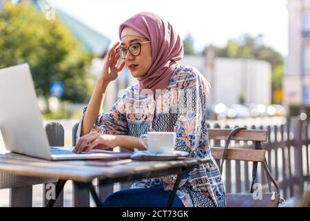 Junge muslimische Frau mit einem Laptop im Café im Freien Stockfoto