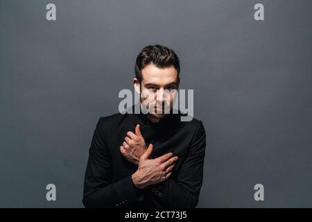Nahaufnahme, Porträt einer jungen gutaussehenden Mann im Anzug, die Hände auf der Brust, in die Kamera schaut, gegen normales studio Hintergrund Stockfoto