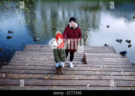 Junge Mutter zu Fuß mit ihrem niedlichen kleinen Tochter draußen in Stadtpark in der Nähe des Flusses Stockfoto