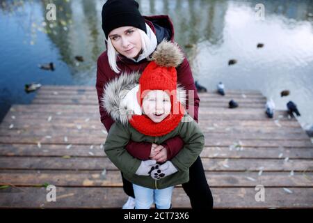 Junge Mutter zu Fuß mit ihrem niedlichen kleinen Tochter draußen in Stadtpark in der Nähe des Flusses Stockfoto