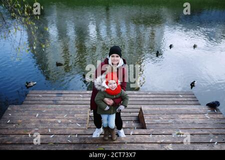 Junge Mutter zu Fuß mit ihrem niedlichen kleinen Tochter draußen in Stadtpark in der Nähe des Flusses Stockfoto