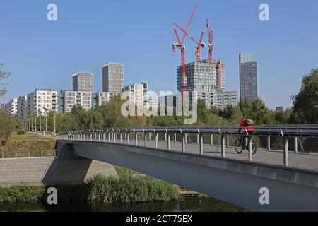 Queen Elizabeth Olympic Park, London. Radfahrer auf East Cross Brücke. Kräne darüber hinaus, da weitere Wohnblöcke auf dem Gelände des Olympischen Dorfes hinzugefügt werden. Stockfoto