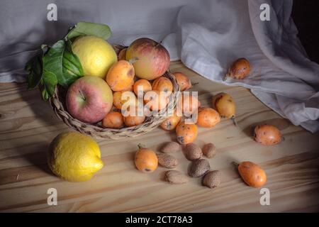 Stillleben in der Ligthmalerei mit einem kleinen Korbkorb mit Früchten, Mispel, Äpfeln, Zitronen und Mandeln in Schale. Stockfoto