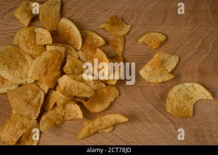 Appetitliche Kartoffelchips sind auf einem Holzbrett verstreut Stockfoto