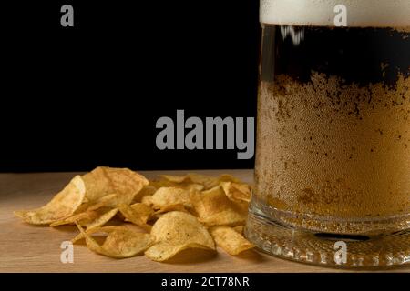 Glas mit Bier und Chips auf einem Holzbrett und Auf schwarzem Hintergrund Stockfoto